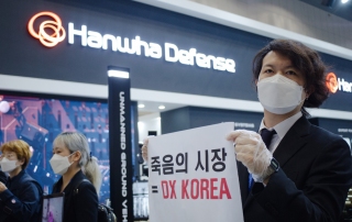 DX 코리아 대응행동에서 참가자가 사신복장을 하고 손에는 "죽음의 시장에 오신 것을 환영합니다"라고 쓰인 피켓을 들고 있다.